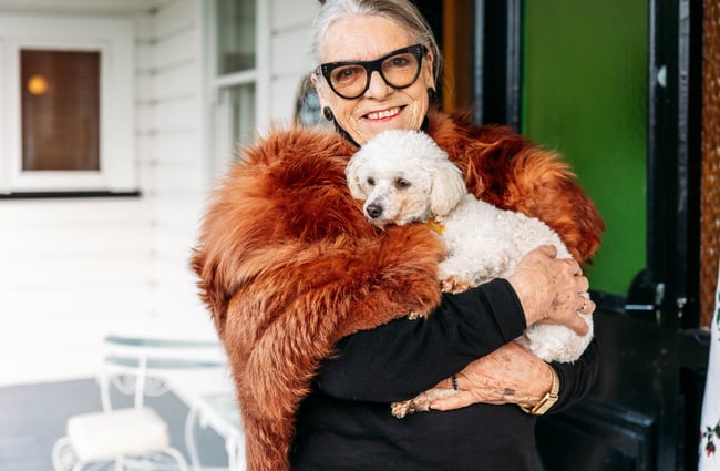 A woman wearing fur holding a dog and smiling to camera.
