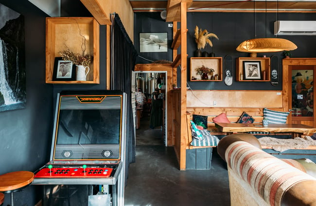 Couch and booth seating inside the Rhyme and Reason taproom with a vintage Tekken machine against one wall.