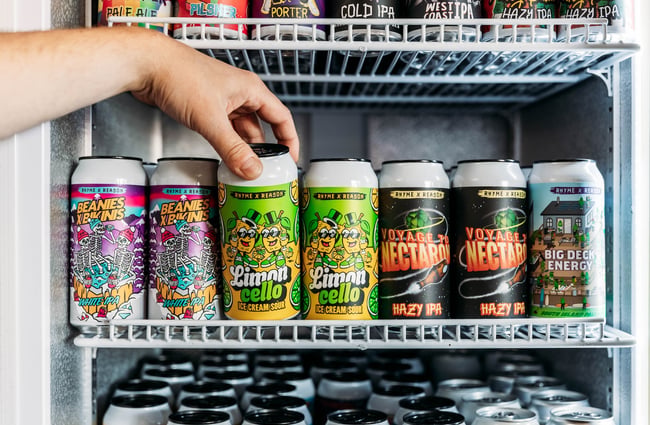 Close up of a hand pulling a can of beer from the neat rows of cans in the fridge.