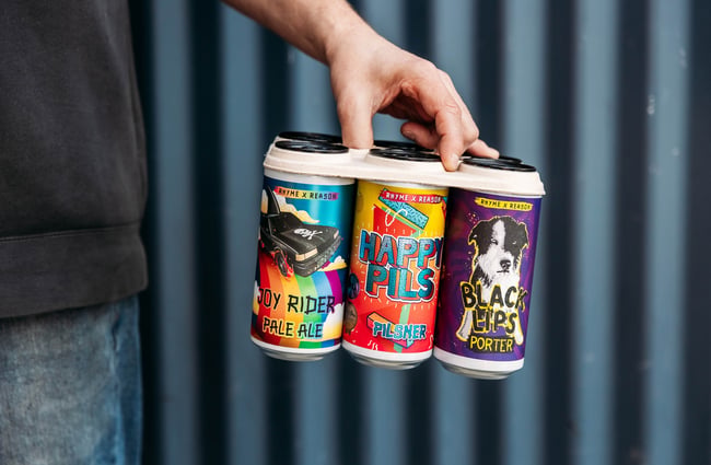 Close up of a hand holding a six-pack of different beers, all with colourful labels.