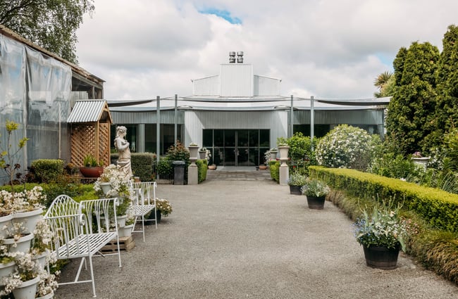 Gravel path leading to silver corrugated iron building with beautiful manicured gardens out front