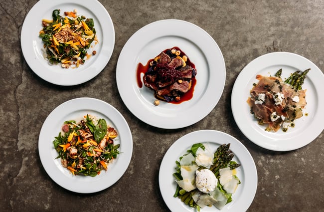 Flat lay of five beautiful plates of food including thai salads, prosciutto, venison and asparagus