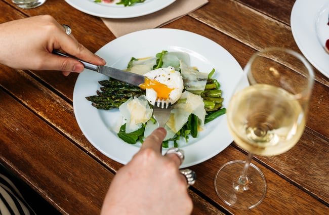 Person cutting into perfectly poached egg on top of shaved parmesan and asparagus