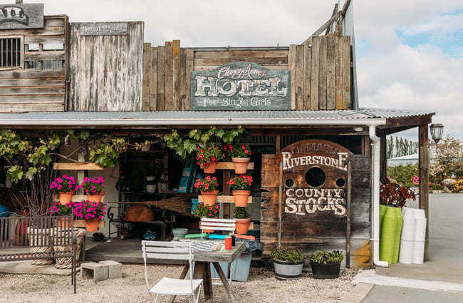 Rustic building with a gold mining aesthetic with flowers and gardening supplies out front