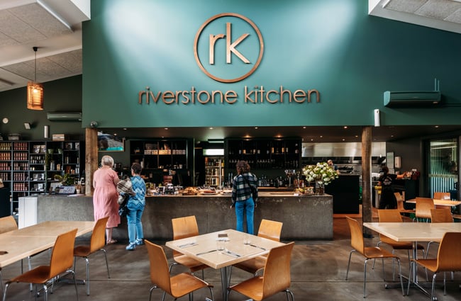Wide shot of Riverstone Kitchen dining room with 3 people looking at cakes and baked goods at the counter