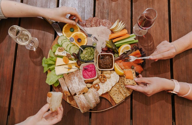 A brids eye view image of a cheese and crackers board with people eating it.