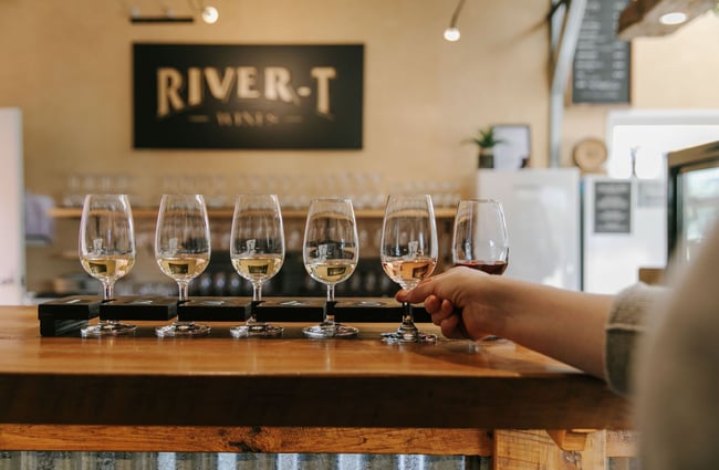 A person reaching up and grabbing wine from a row of wine glasses on the bar.