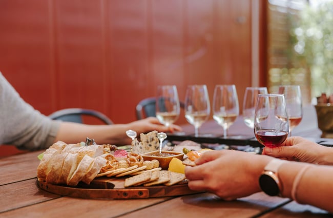 People sitting around an outside table eating a cheese board and doing a wine tasting.