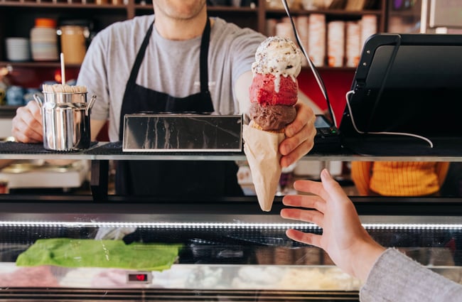 Man passing a customer a triple cone ice cream.