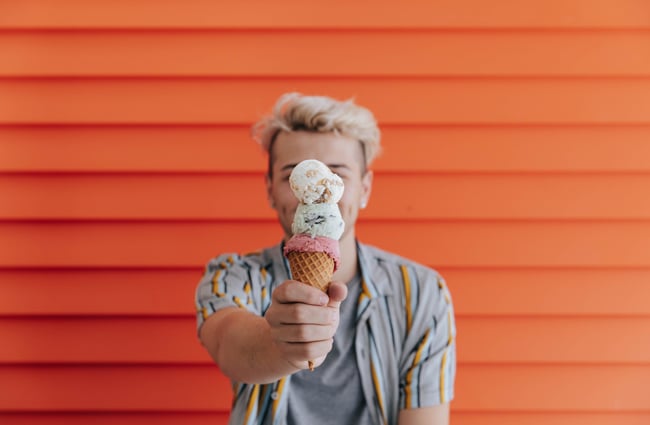 Double scoop gelato on a cone in front of an orange wall.