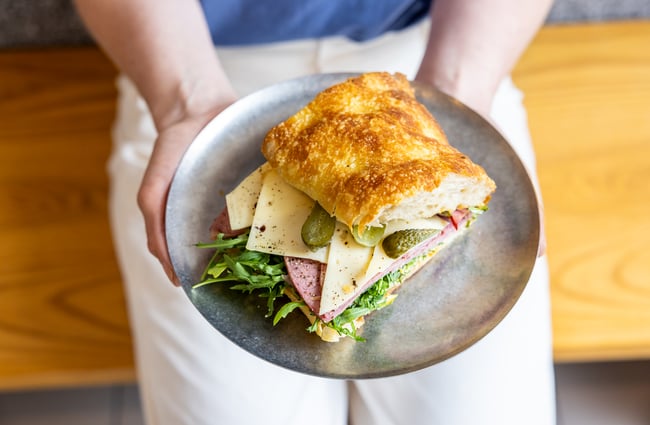 A person's hand holds a sandwich on a plate at Rook.