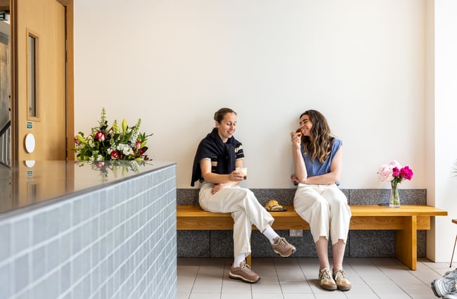 Two customers are sitting on a bench talking and drinking coffee at Rook.