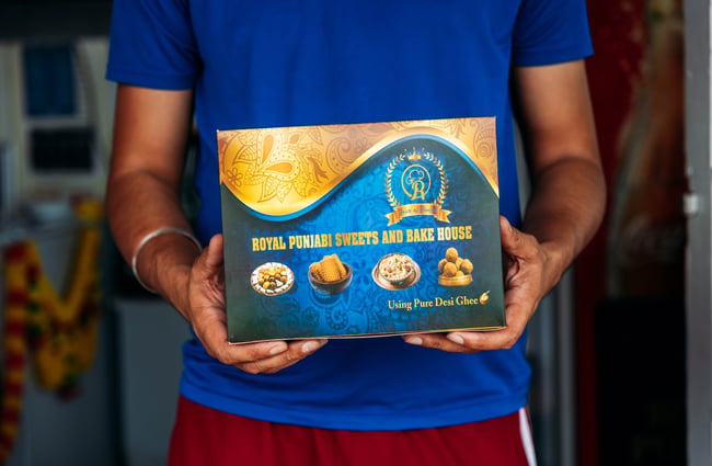 Shopkeeper holding a box at Royal Punjabi Sweets and Bake House.