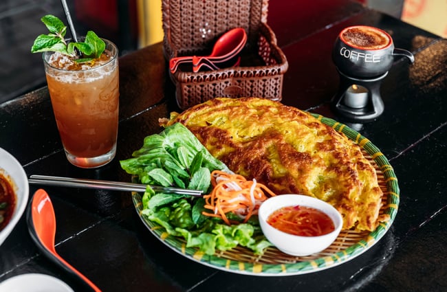 A Vietnamese pancake is on the table with a cocktail at Saigon '60s.