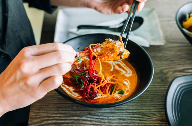 Close up of someone using chop sticks to pick up food on a plate.