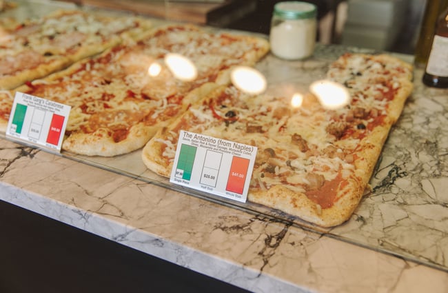 An image looking into the glass cabinet where there are different pizzas on display.