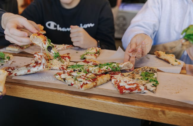 People sitting around a table with a pizza in the middle all sharing.