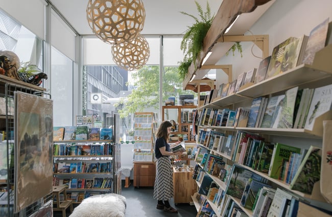 A woman looks through a book near a large window inside Scorpio Books.