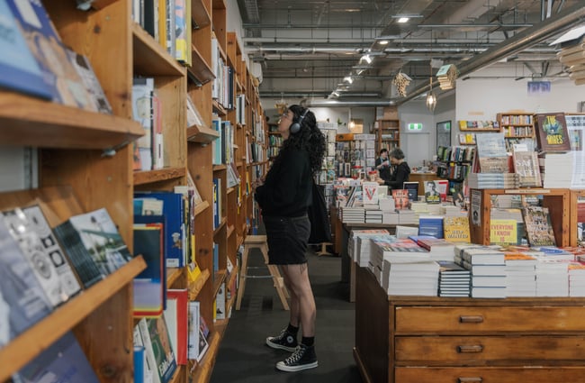 A woman wearing headphones looks at book titles on a shelf.