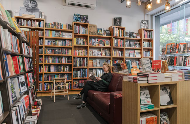 A woman sitting on a dark brown leather couch reading a book, surrounded by bookshelves, in Scorpio Books.