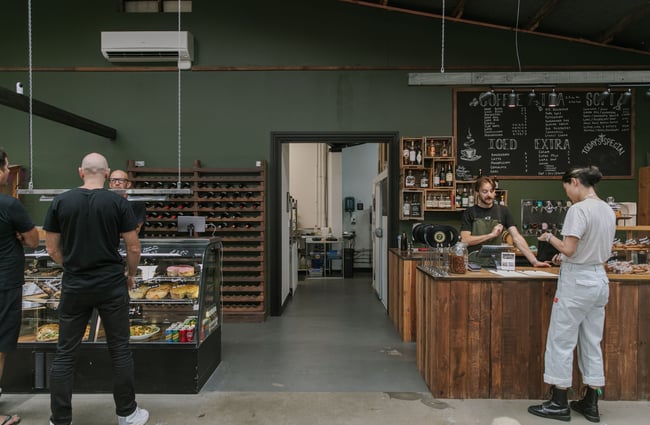 Customers standing around at a counter inside a green decorated cafe.