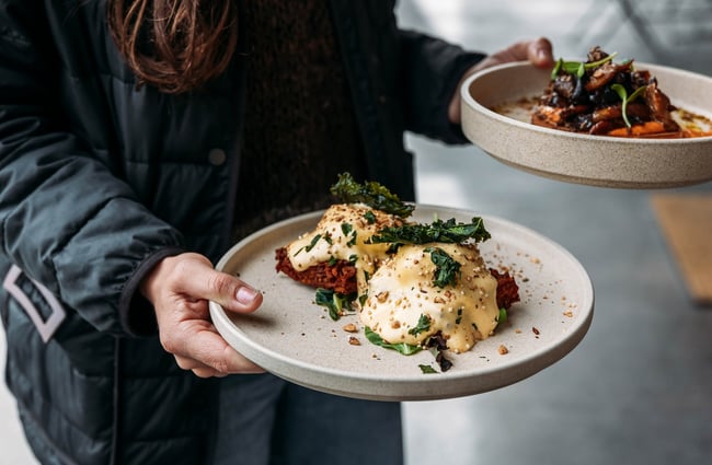 Close up of a waiter holding one savoury dish in each hand.