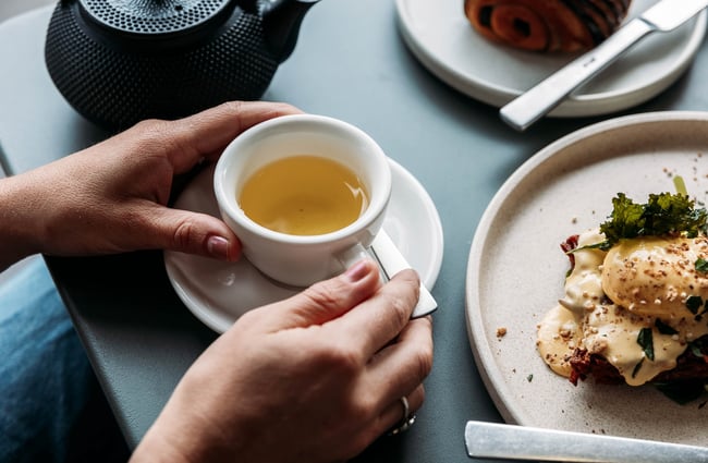 Close up of a person's hands wrapped around a small mug of green tea.