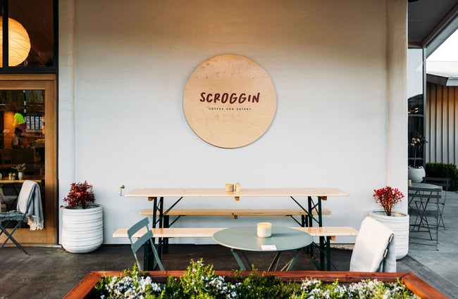 Exterior seating area at Scroggin, Wānaka, below a round, wooden Scroggin sign on the exterior wall.