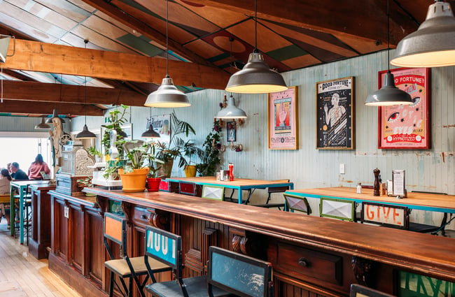 A long wooden leaner with mismatched chairs in the interior dining area of Seashore Cabaret.