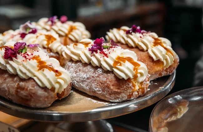 Close up of cream-filled donuts, sprinkled with pink flowers, on a silver cake stand at Seashore Cabaret.