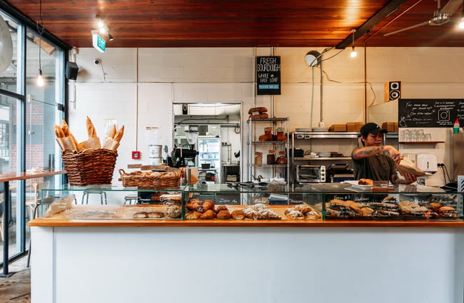 Overview of bakery cabinet with baguettes on top and pastries and sandwiches inside