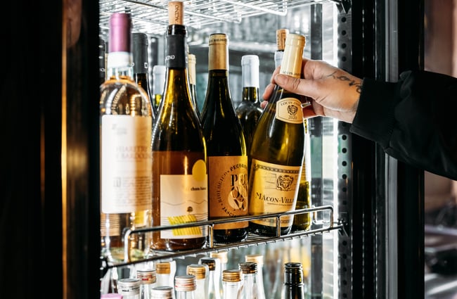 A hand grabbing a bottle of wine wine in a fridge.