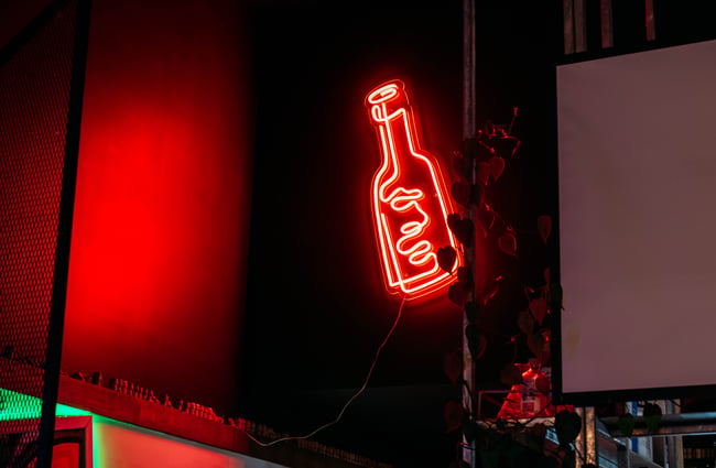 A bright orange fluorescent sign resembling a bottle on a wall.