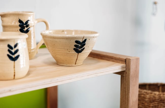 Close up of ceramic bowl with a beige speckled glaze and painted plant details