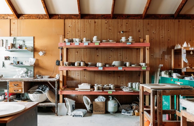 Pottery studio with in progress works sitting on shelf next to a workshop space splattered in clay