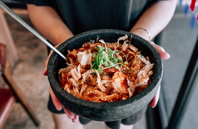 Woman holding a bowl of Korean prawns and noodles from Simon and Lee, Auckland.