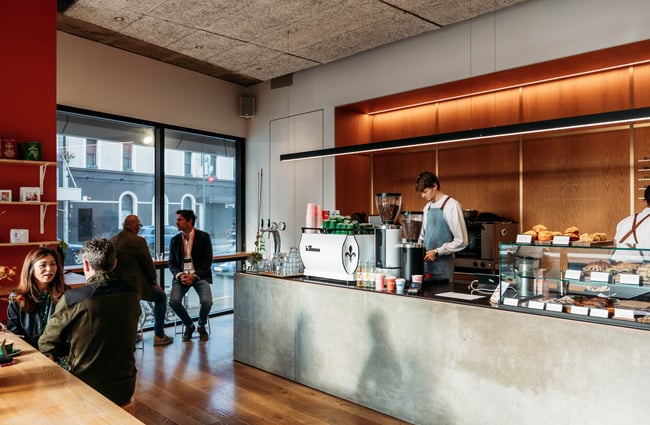 Customers sitting at tables and barista behind coffee machine at Sketchbook Coffee.