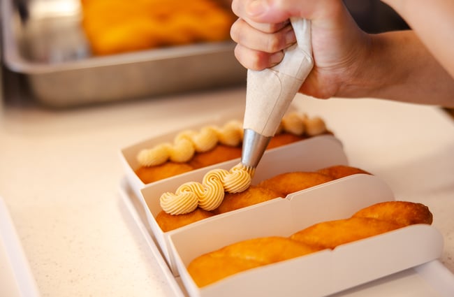 Icing being squeezed on to long slim donuts.