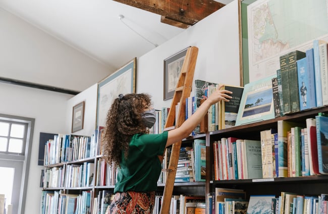 Woman up a ladder looking for books at Smith's Bookshop, Christchurch.