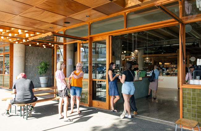 People hanging outside a cafe with large glass windows and doors.