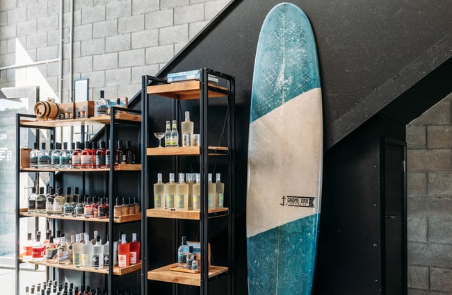 Bottles of gin on shelves next to a surfboard.