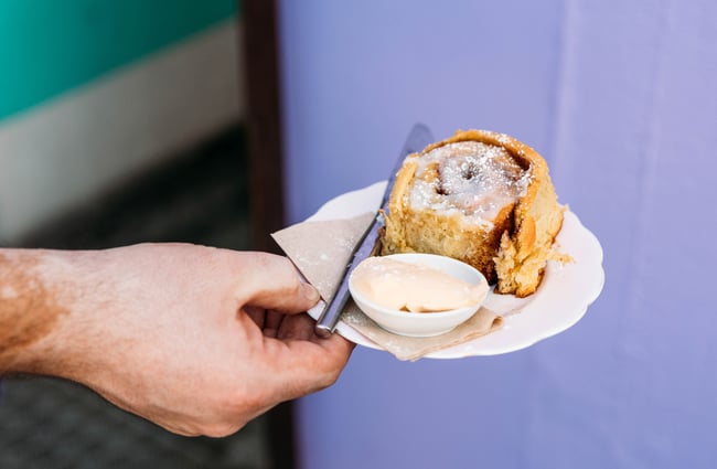 A hand holding out a plate with a cinnamon scroll at Space Cadet, Hamilton.