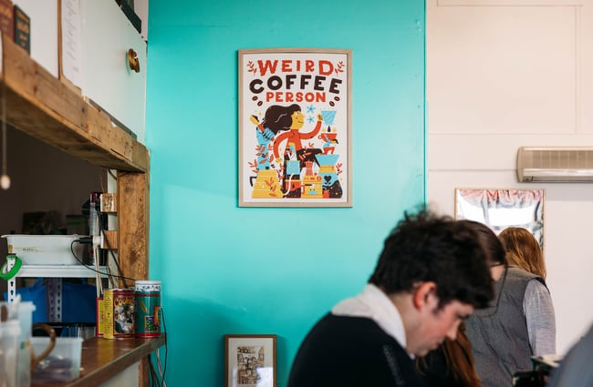 Framed coffee person artwork on a bright blue wall at Space Cadet, Hamilton.