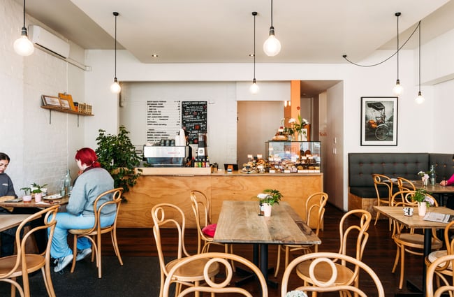 Customers seating at wooden tables and chairs inside a brightly lit cafe.