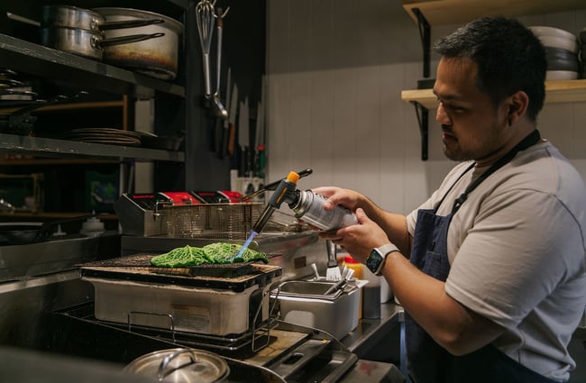 A chef using a blowtorch on cabbage leaves.