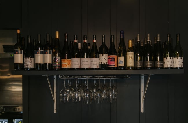 Wine bottles arranged on a shelf and wine glasses hanging below it at Story.