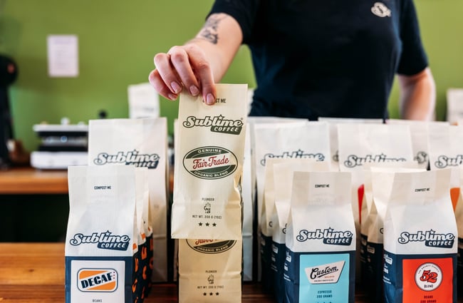A hand is lifting up a bag of coffee beans on display at Sublime Coffee Roasters.