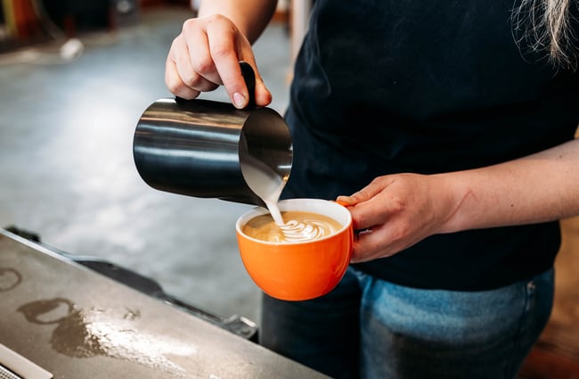 Barista pouring steamed milk into a cup of coffee at Sublime Coffee Roasters.