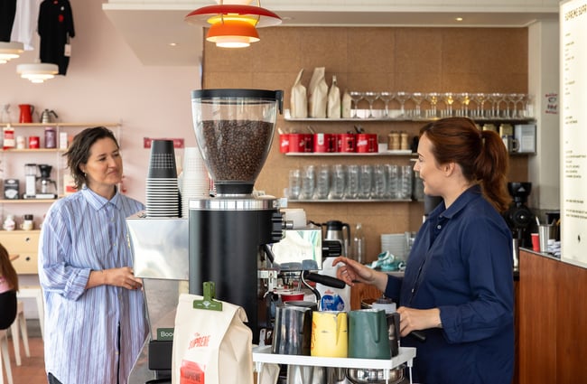 A customer is at the front counter talking to the barista behind the coffee machine at Supreme Supreme.