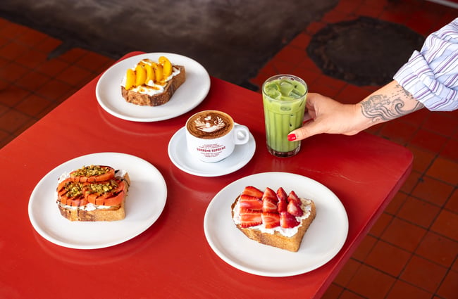 A table with multiple food dishes, coffee and a smoothie at Supreme Supreme.